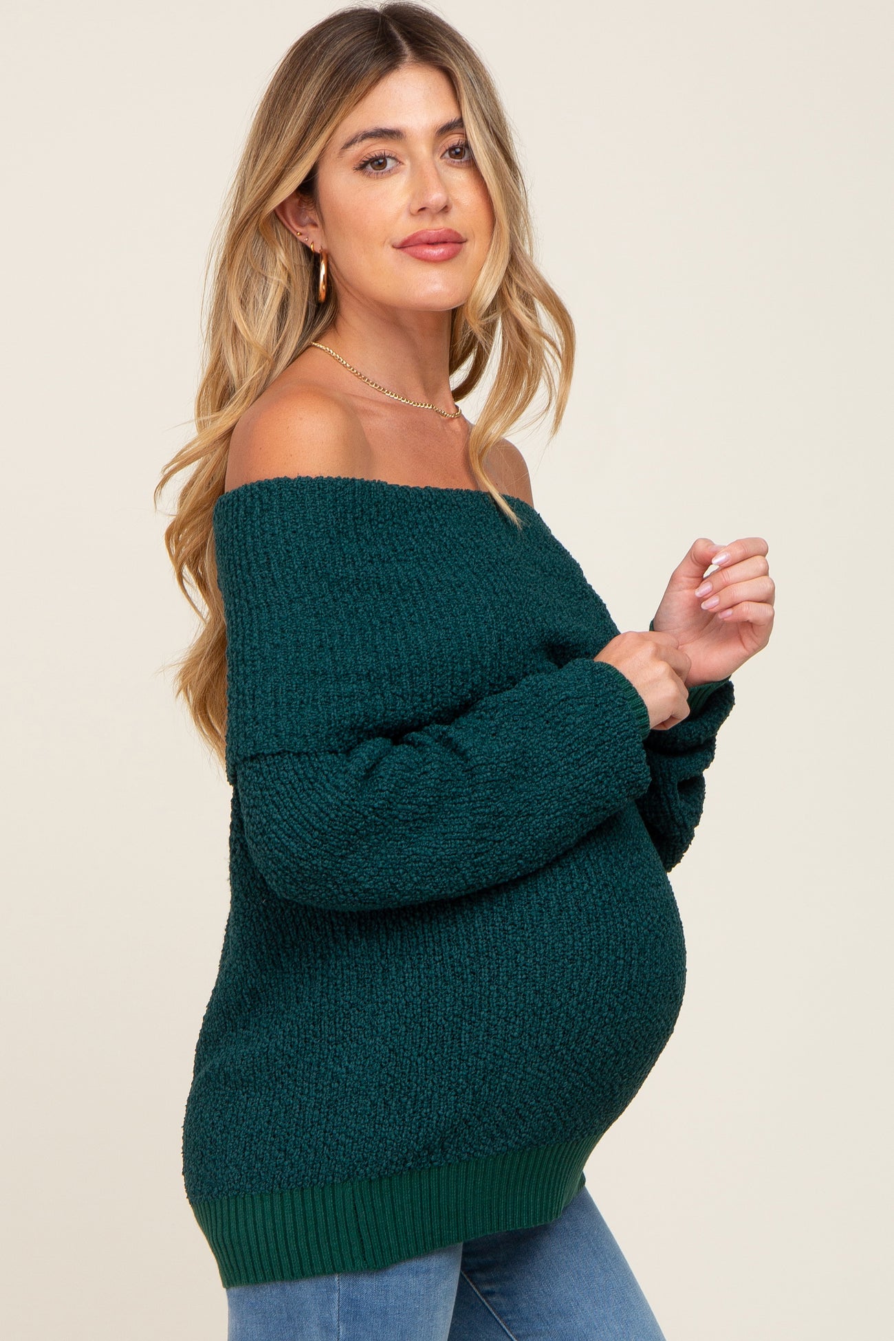 woman wearing a dark green off-the-shoulder maternity sweater with long sleeves and a visible baby bump