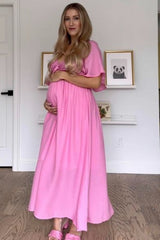 woman wearing a pink maternity dress with short sleeves and a gathered waist, holding her baby bump