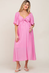woman wearing a pink maternity dress with a tie front and short flutter sleeves, holding her baby bump