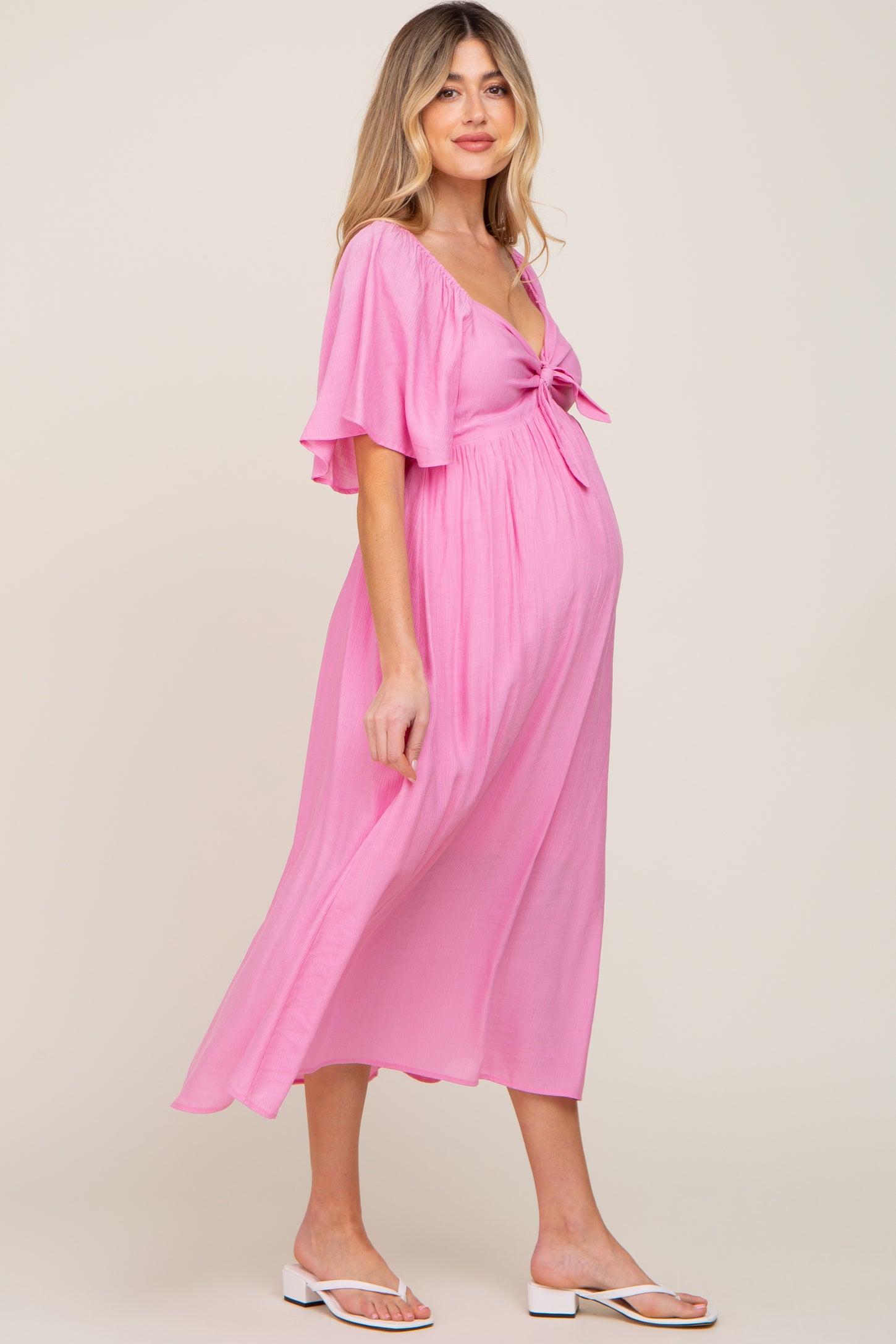 woman wearing a pink maternity dress with short flutter sleeves and a tie front, showcasing her baby bump