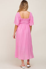 woman wearing a pink maternity maxi dress with a smocked bodice and short flutter sleeves, back view