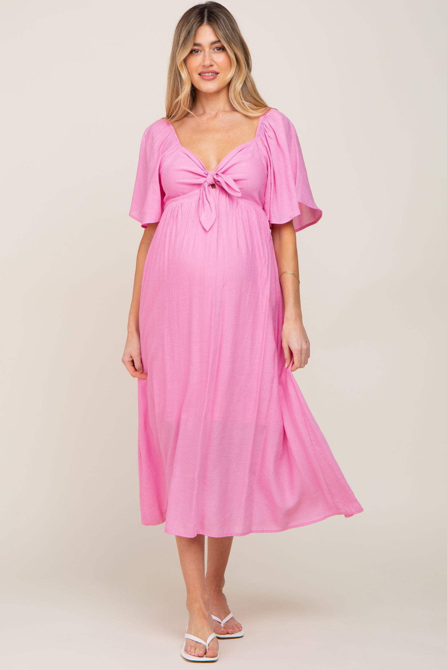 woman wearing a pink maternity dress with a tie front and short sleeves, highlighting her baby bump