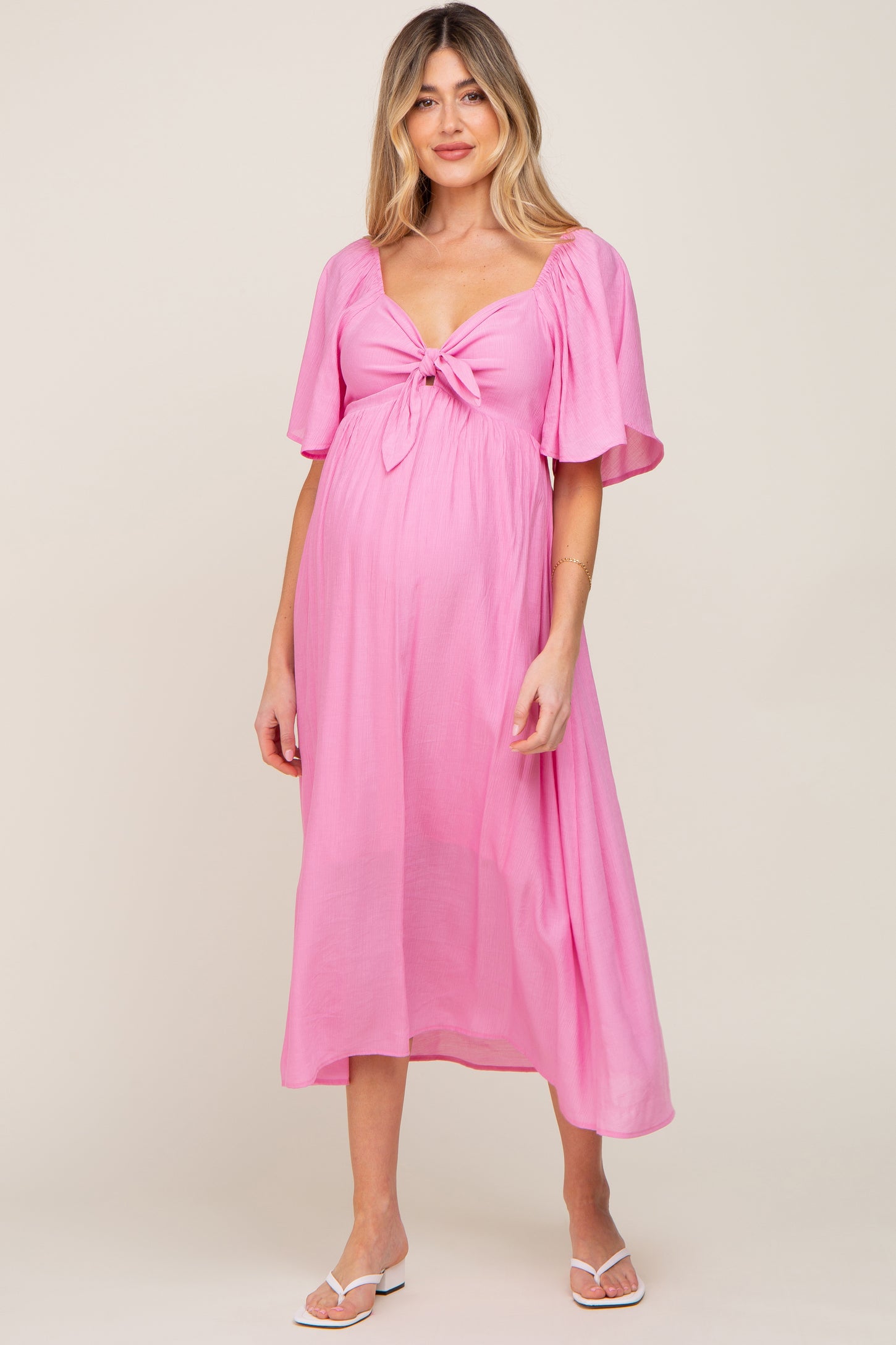 woman wearing a pink maternity dress with a tie front, short sleeves, and a flowing skirt, highlighting her baby bump