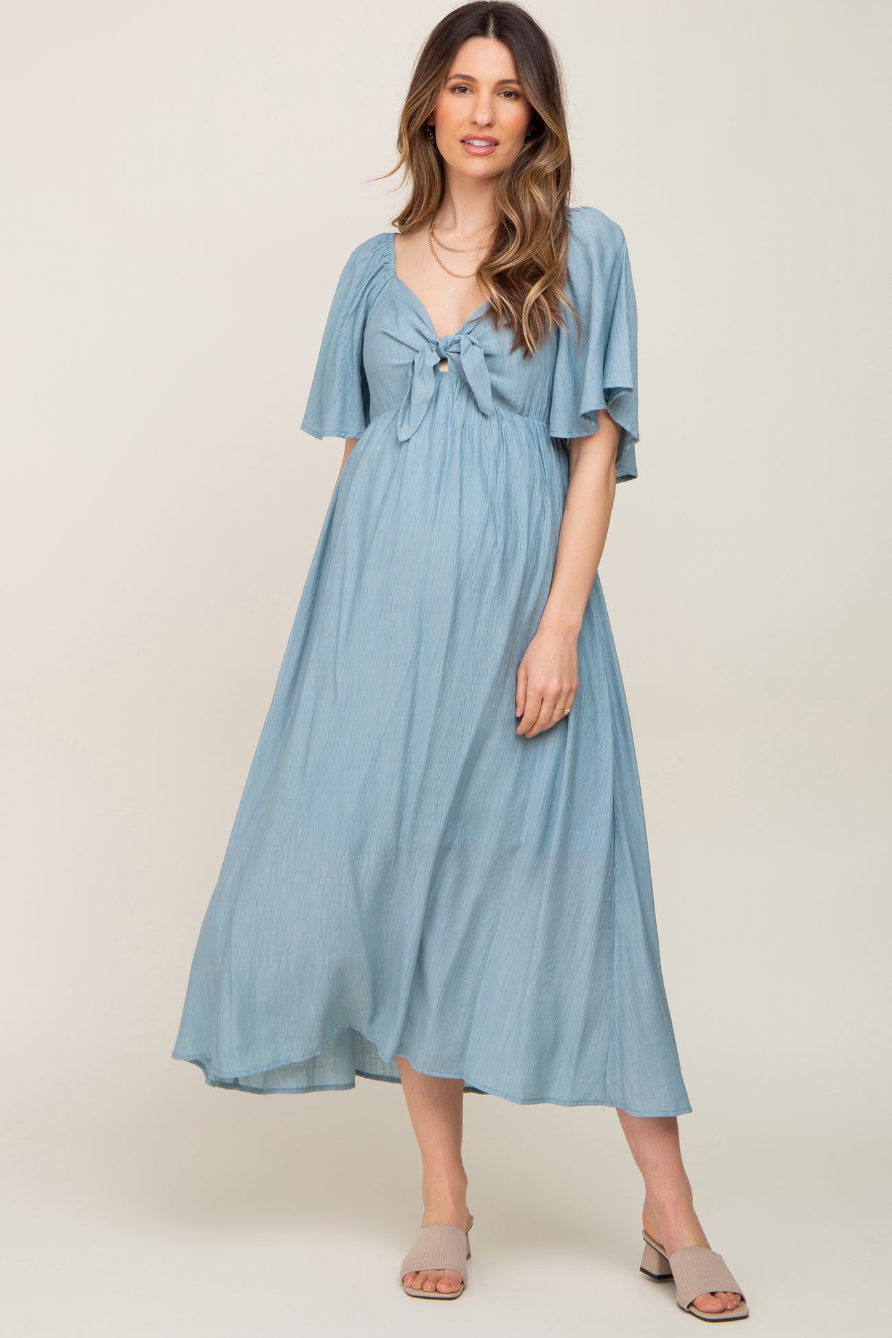 woman wearing a light blue maternity maxi dress with a tie-front and flutter sleeves, showcasing a baby bump