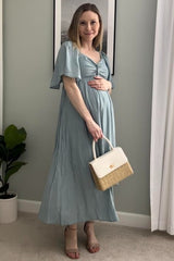 woman wearing a light blue maternity maxi dress and holding her baby bump, carrying a white handbag