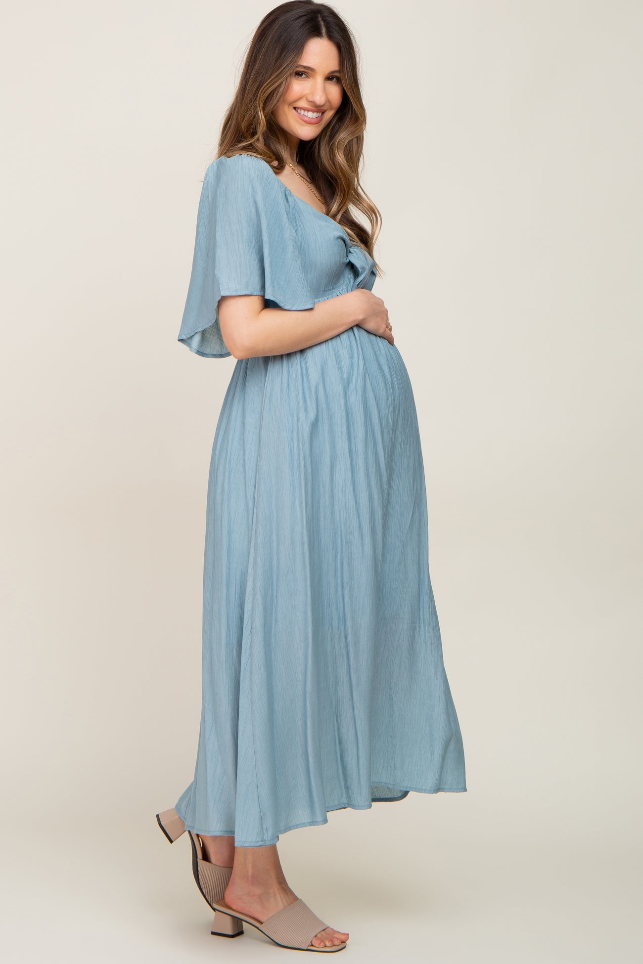 woman wearing a light blue maternity maxi dress and holding her baby bump