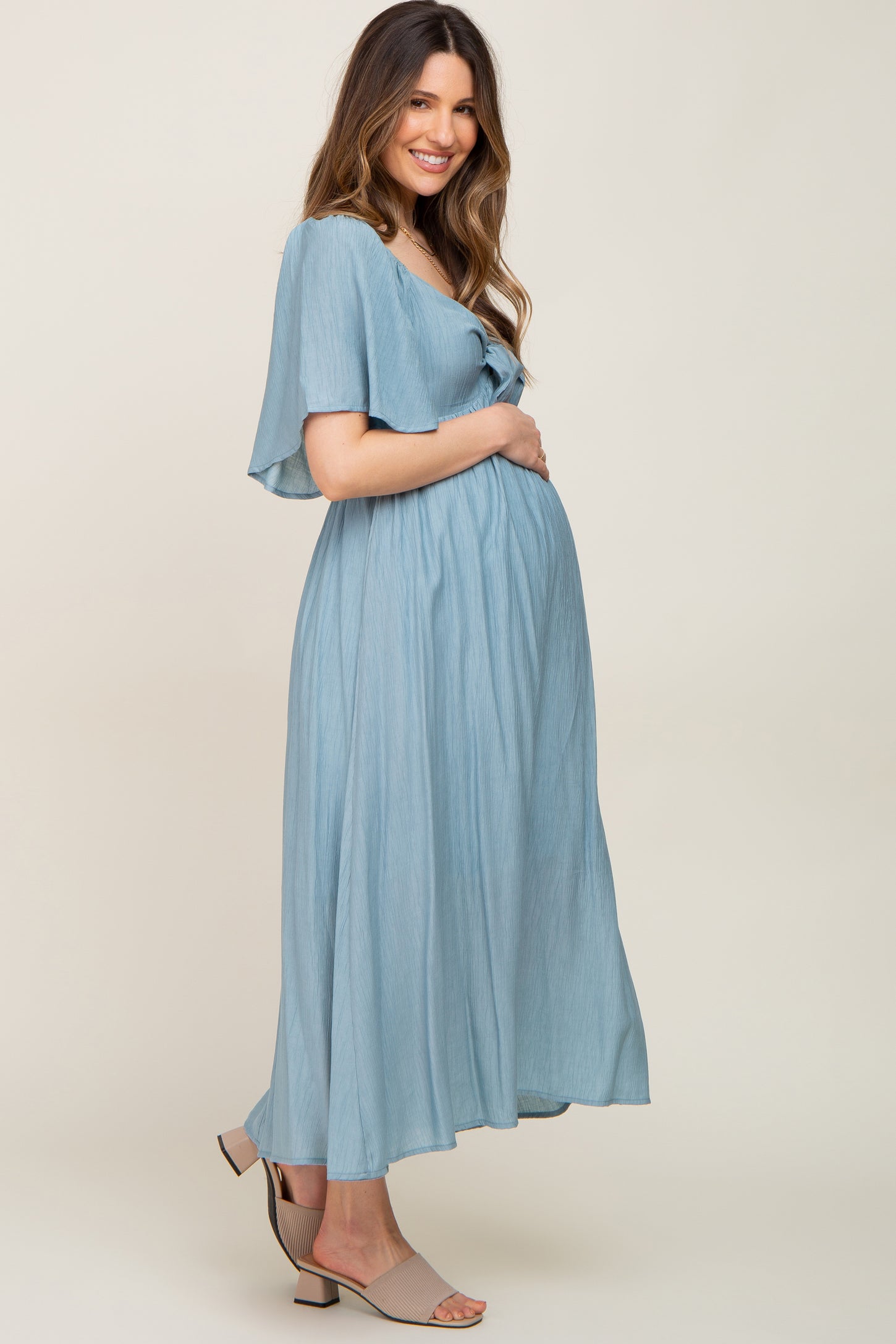 woman wearing a light blue maternity maxi dress and holding her baby bump