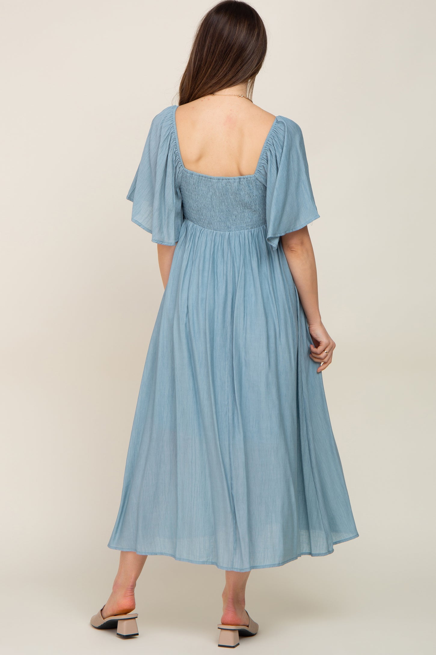 woman wearing a light blue maternity dress with flutter sleeves and a fitted bodice, showing the back view