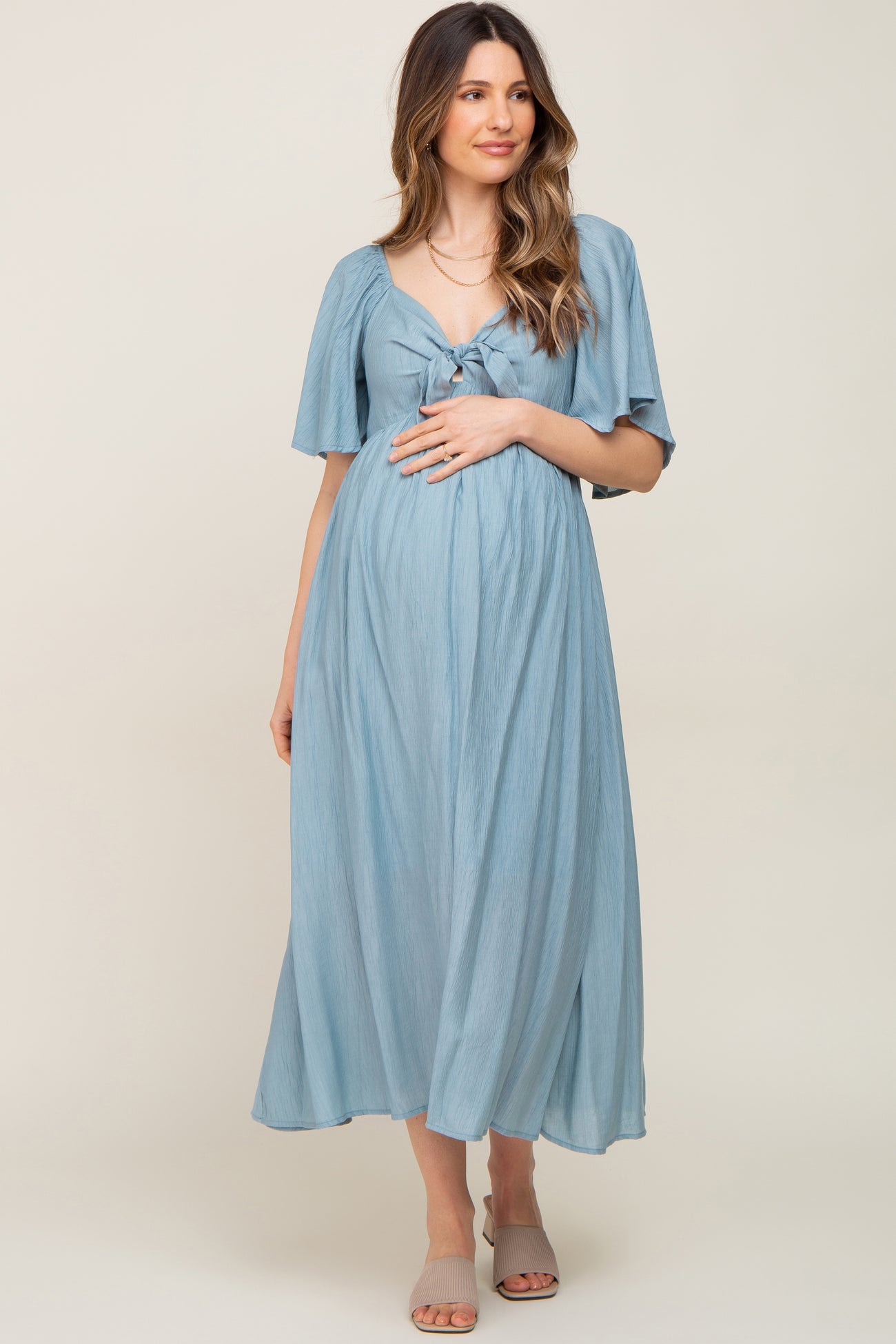 woman wearing a light blue maternity dress with a tied front and flutter sleeves, gently cradling her baby bump