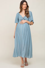 woman wearing a light blue maternity dress with a tied front and flutter sleeves, gently cradling her baby bump