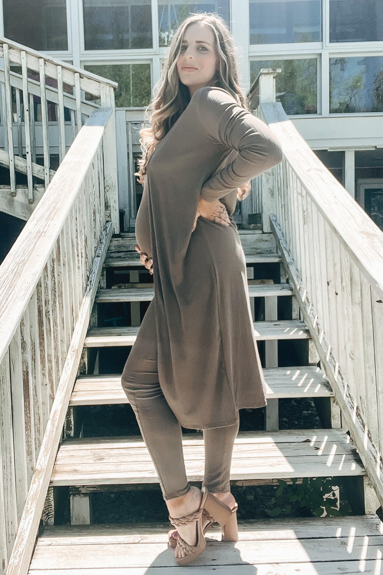 pregnant woman in brown maternity set and cardigan posing on wooden stairs