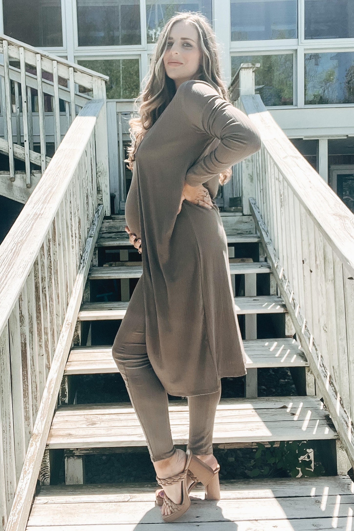 pregnant woman in brown maternity set and cardigan posing on wooden stairs