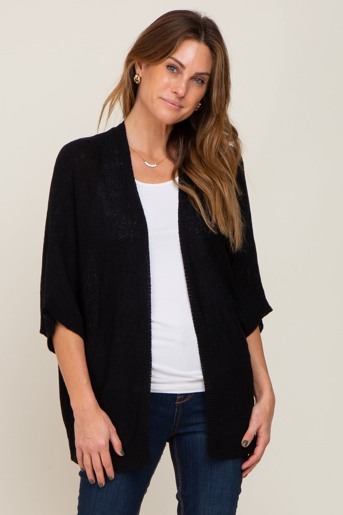 woman wearing a black short sleeve open front cardigan over a white shirt and blue jeans