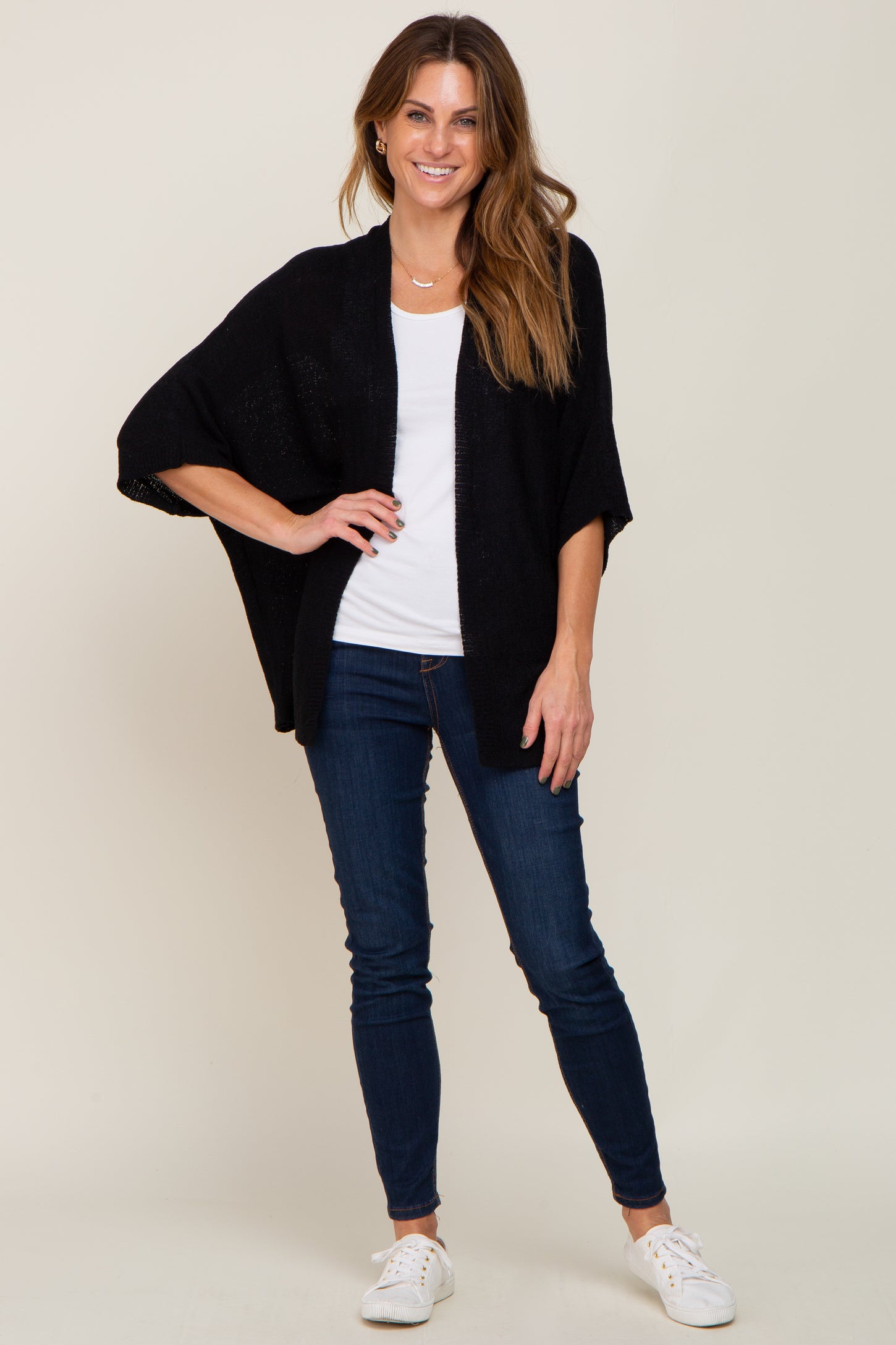 woman wearing a black open-front cardigan over a white t-shirt with dark skinny jeans and white sneakers