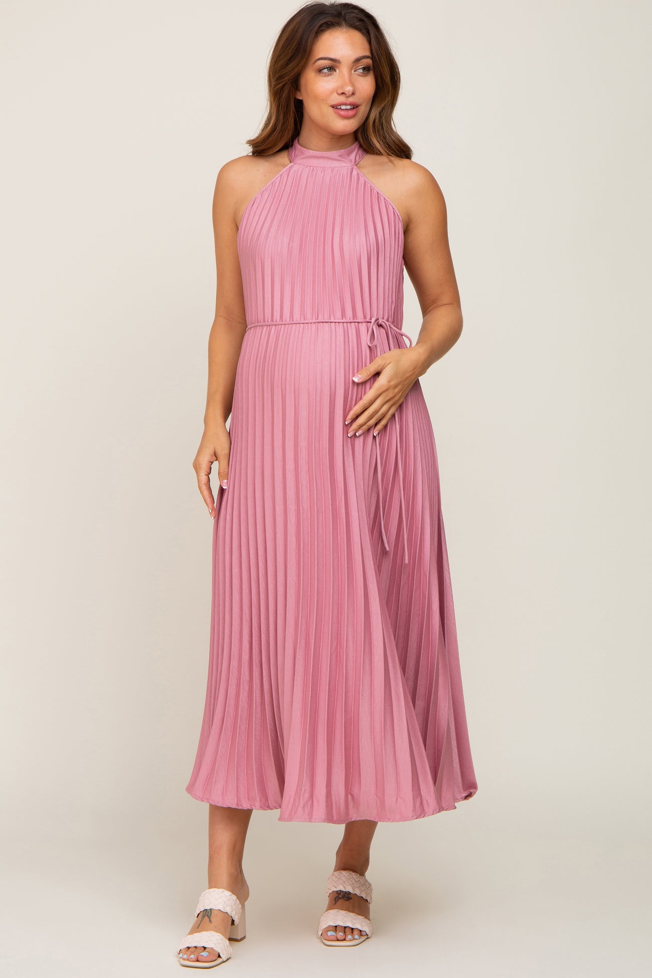 woman wearing a pink pleated maternity dress with a halter neckline and tied waist, displaying a baby bump