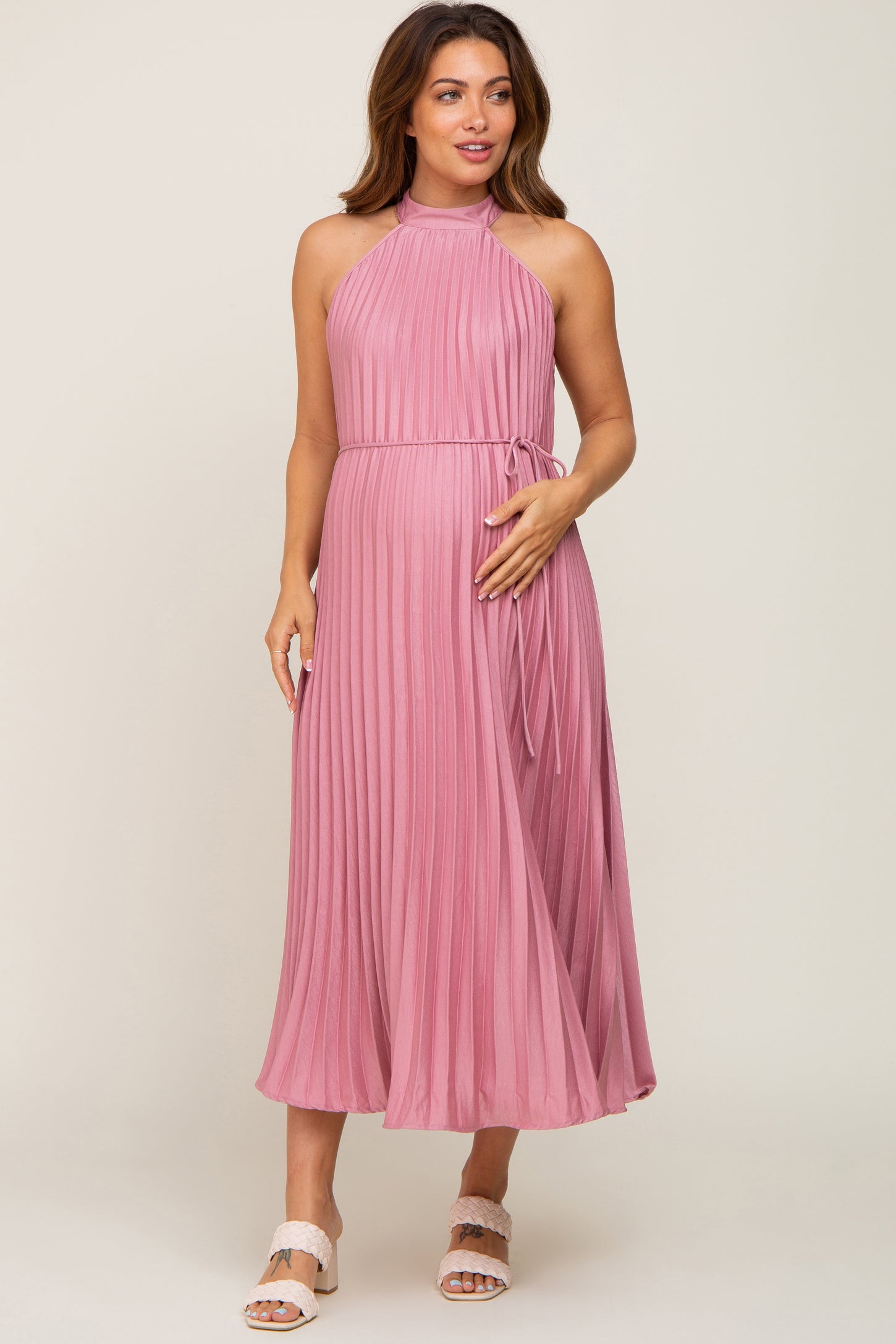 woman wearing a pink pleated maternity dress with a halter neckline and tied waist, displaying a baby bump