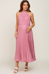 woman wearing a pink pleated maternity dress with a halter neckline and tied waist, displaying a baby bump
