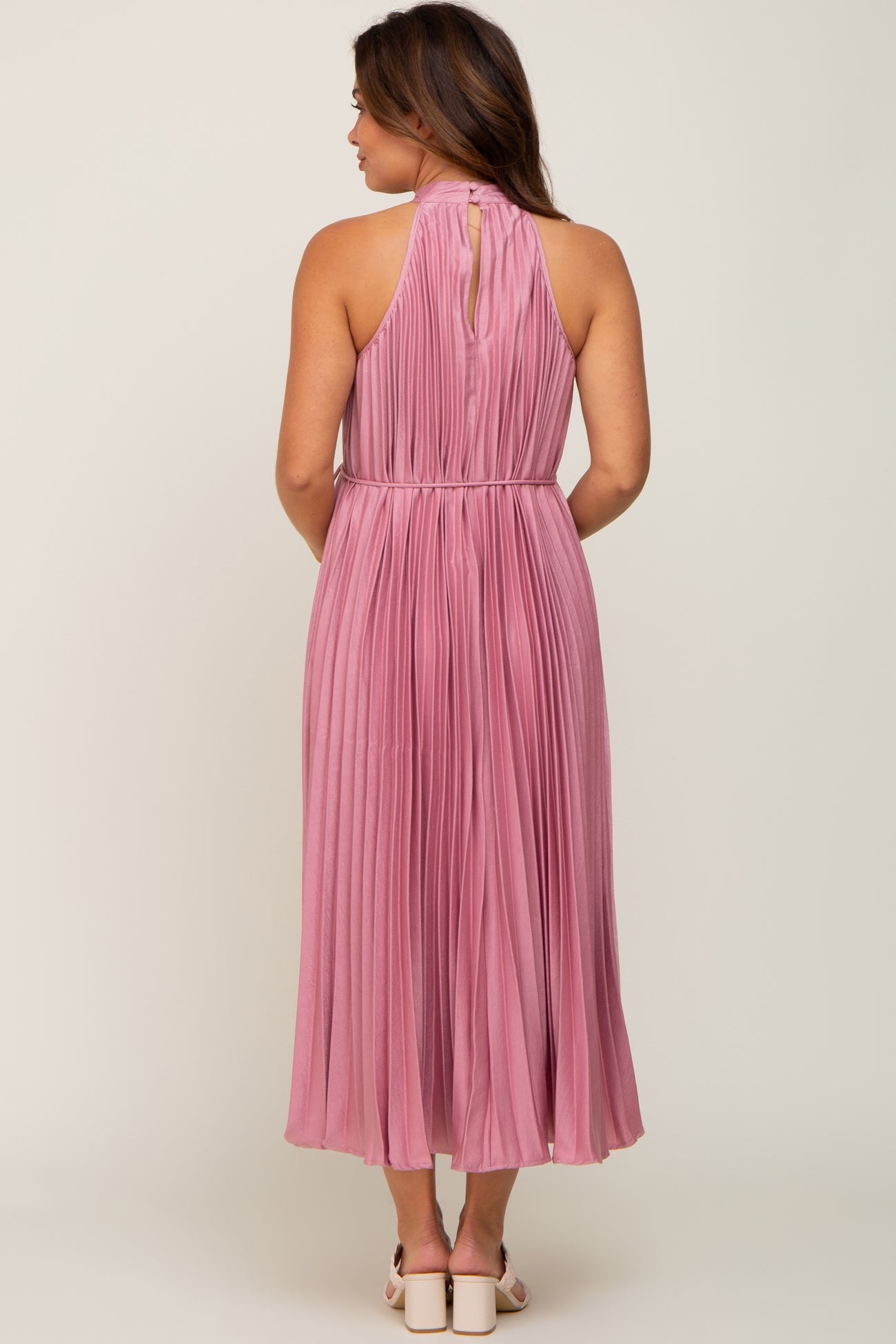 maternity wear long pink pleated dress with a halter neck and a keyhole back detail, model facing away from the camera