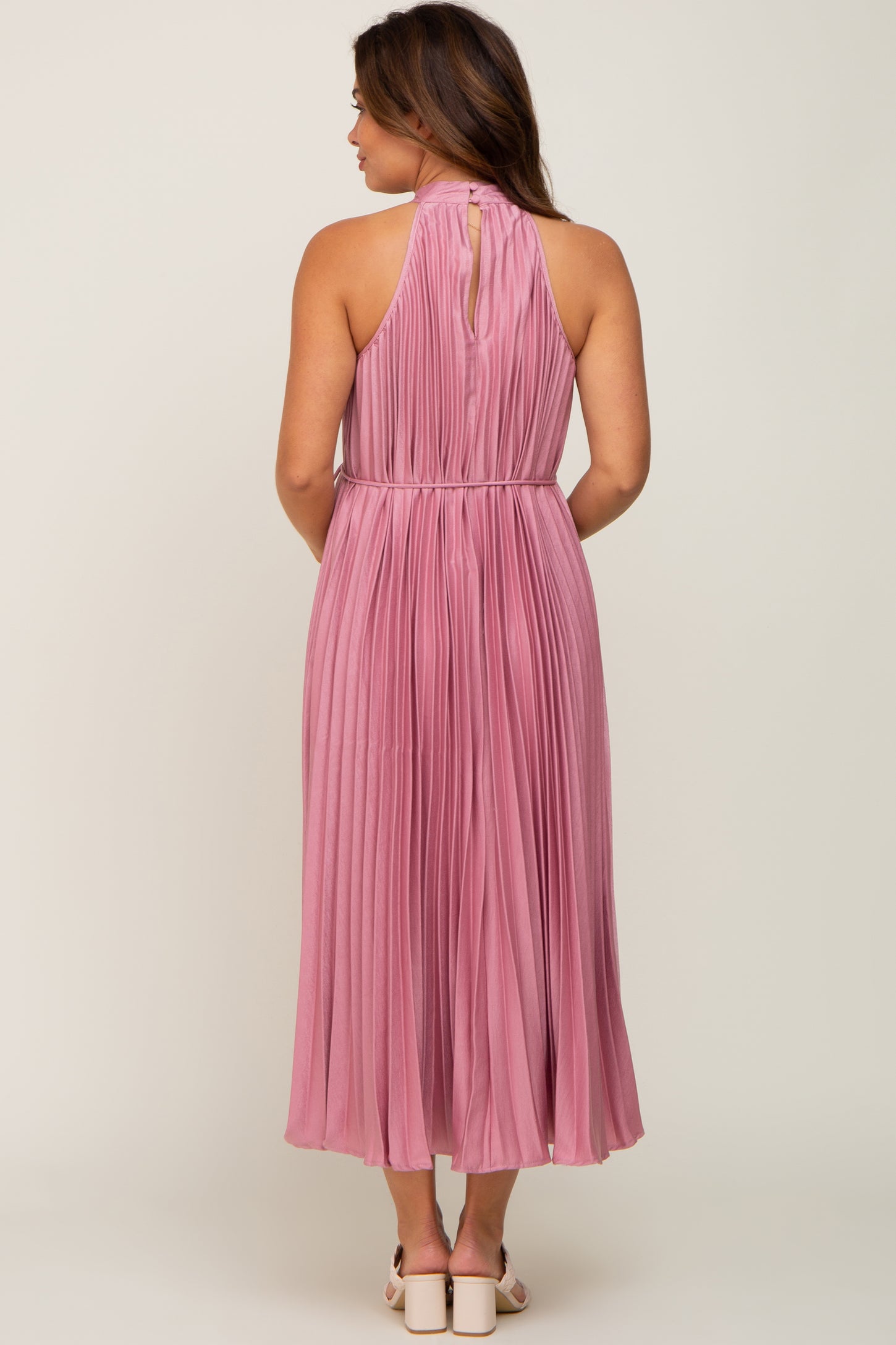 maternity wear long pink pleated dress with a halter neck and a keyhole back detail, model facing away from the camera