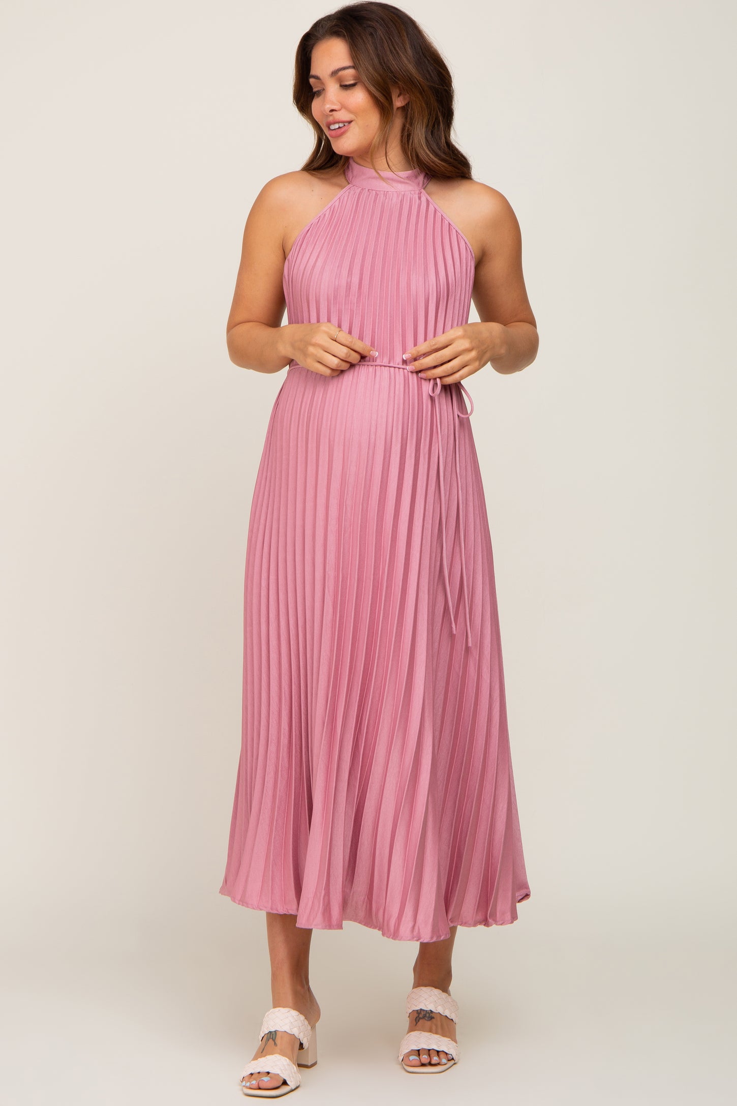 woman wearing a pink pleated maternity dress with a halter neckline and a tie at the waist
