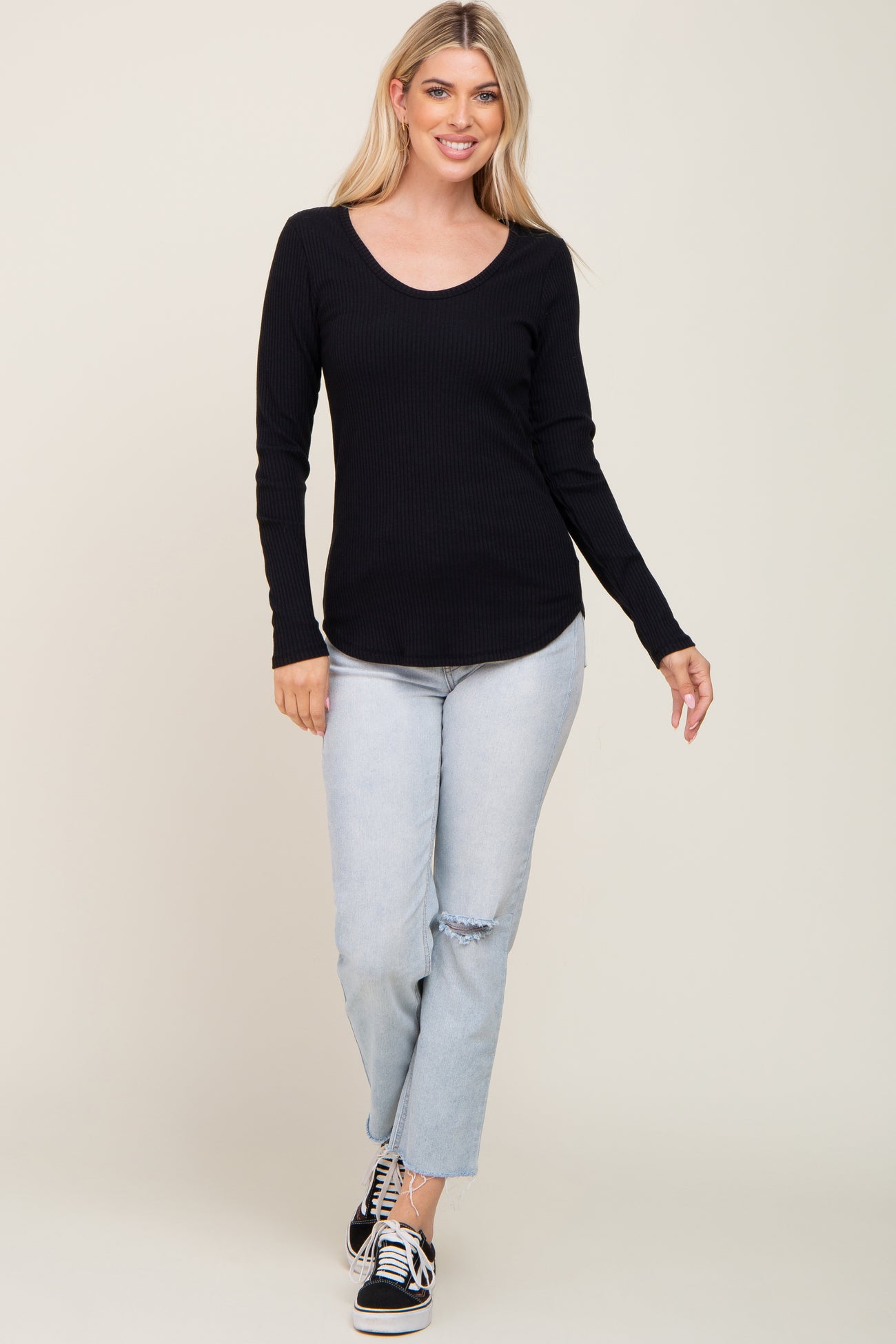 woman wearing a black ribbed long sleeve top and light blue ripped jeans, walking and smiling