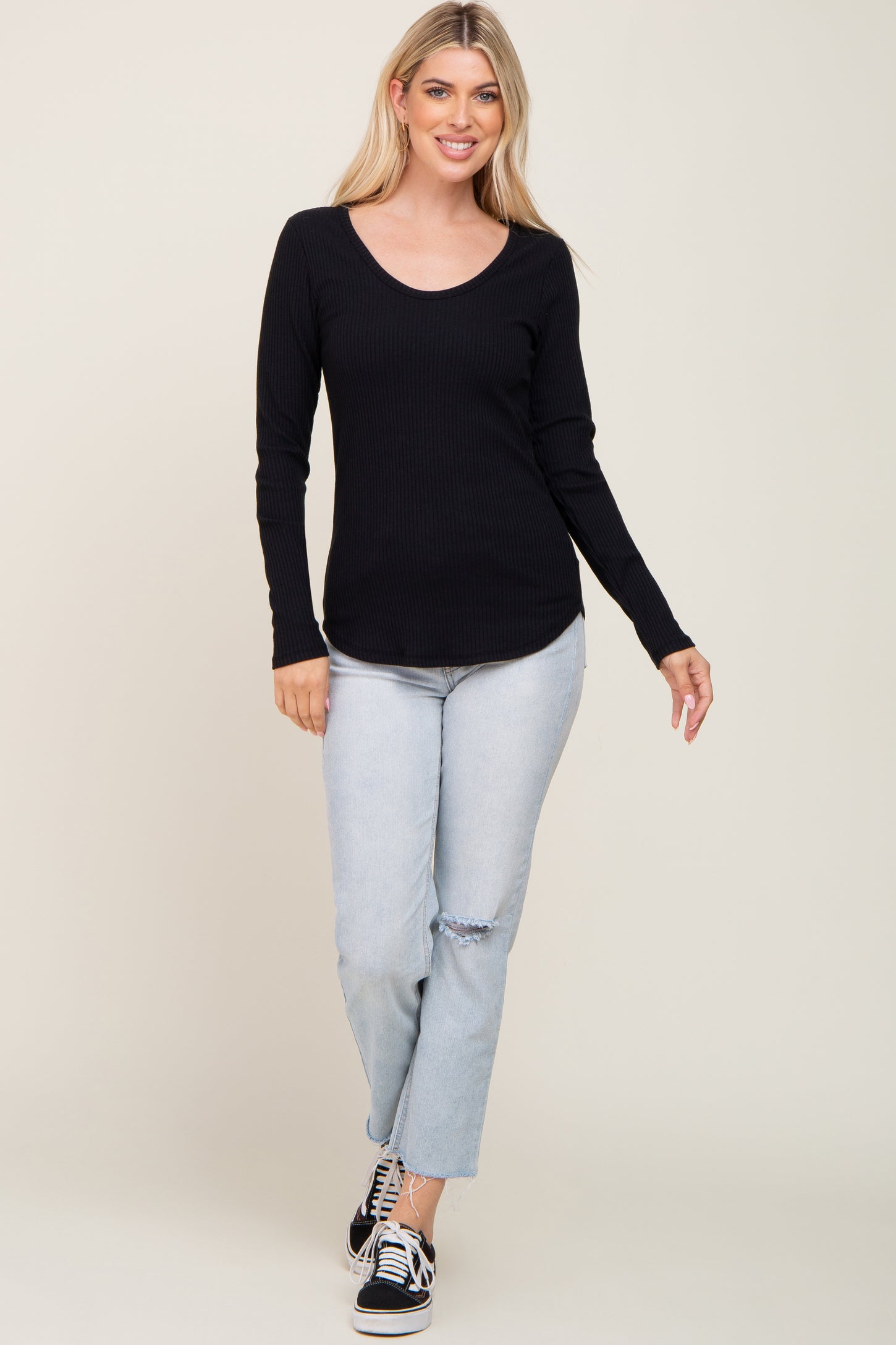 woman wearing a black ribbed long sleeve top and light blue ripped jeans, walking and smiling