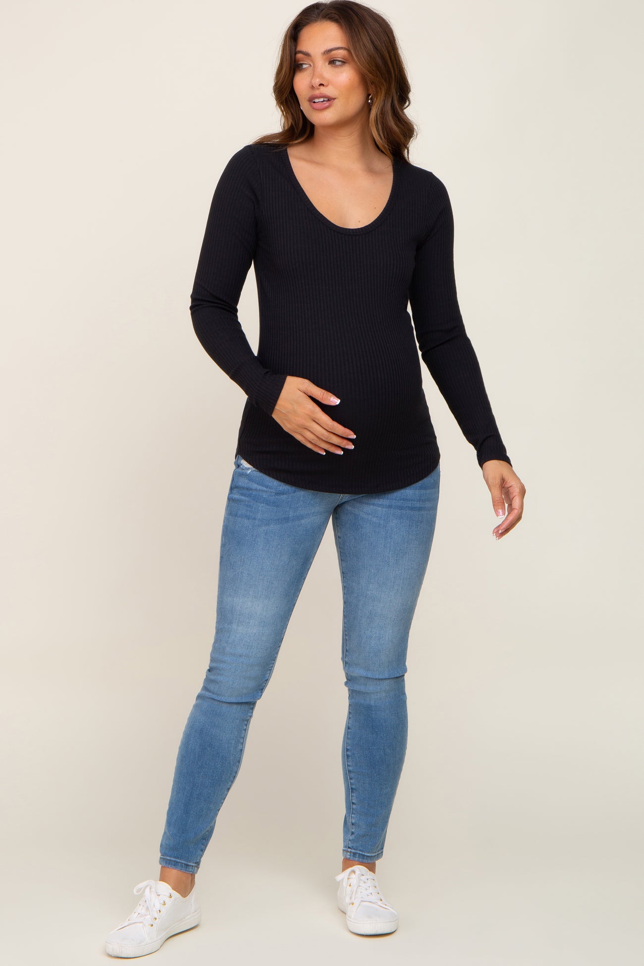 woman wearing a black ribbed maternity top with a v-neck and long sleeves, holding her baby bump, paired with blue jeans
