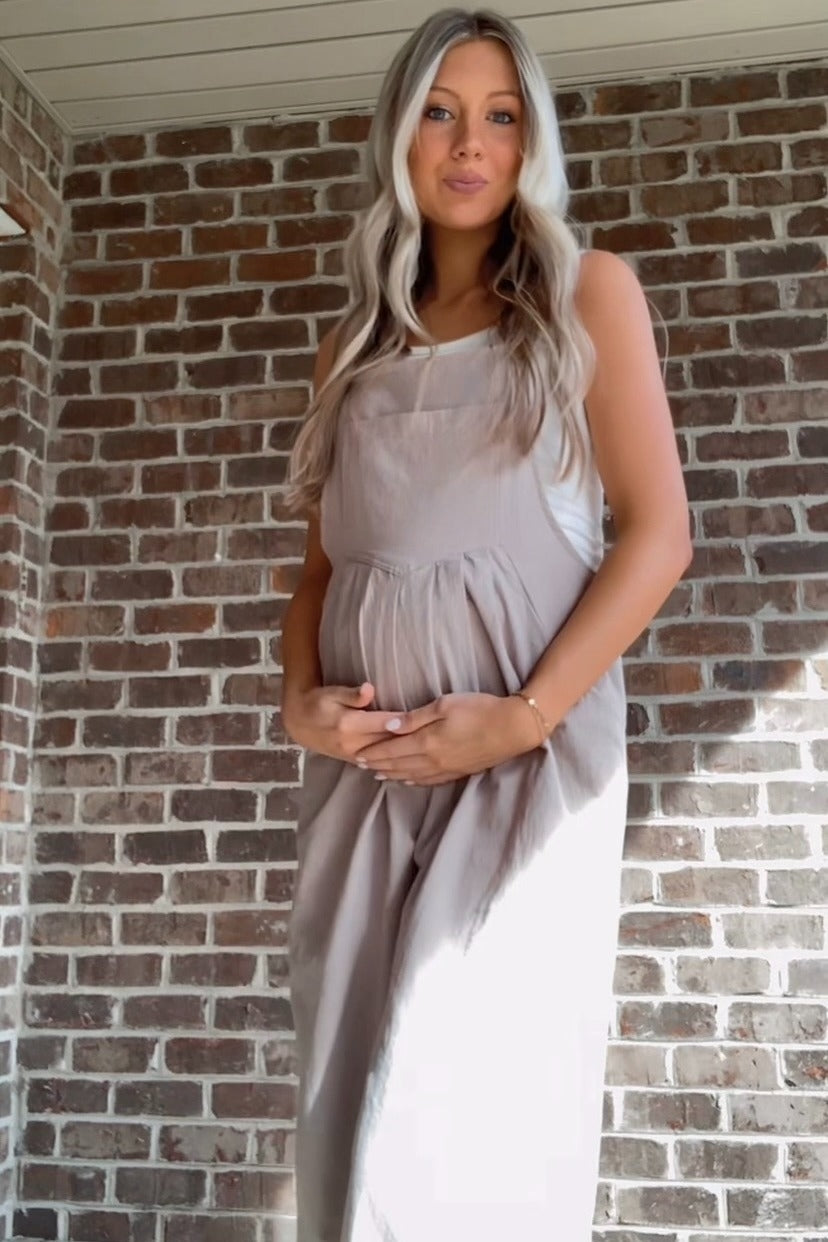 woman wearing a beige maternity dress and holding her baby bump against a brick wall background