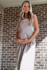 woman wearing a beige maternity dress and holding her baby bump against a brick wall background
