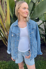 woman wearing a light blue maternity denim jacket over a white tank top, with a visible baby bump and denim shorts