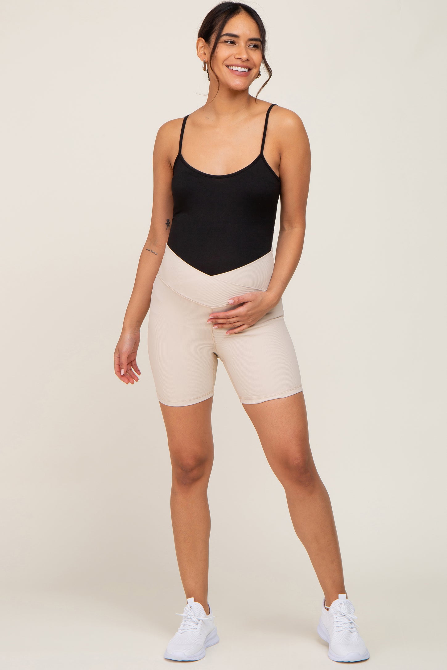 woman wearing a black maternity bodysuit and beige maternity bike shorts, showing her baby bump