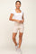 woman wearing a white square neck crop top and beige biker shorts, posing with a smile and gray sneakers