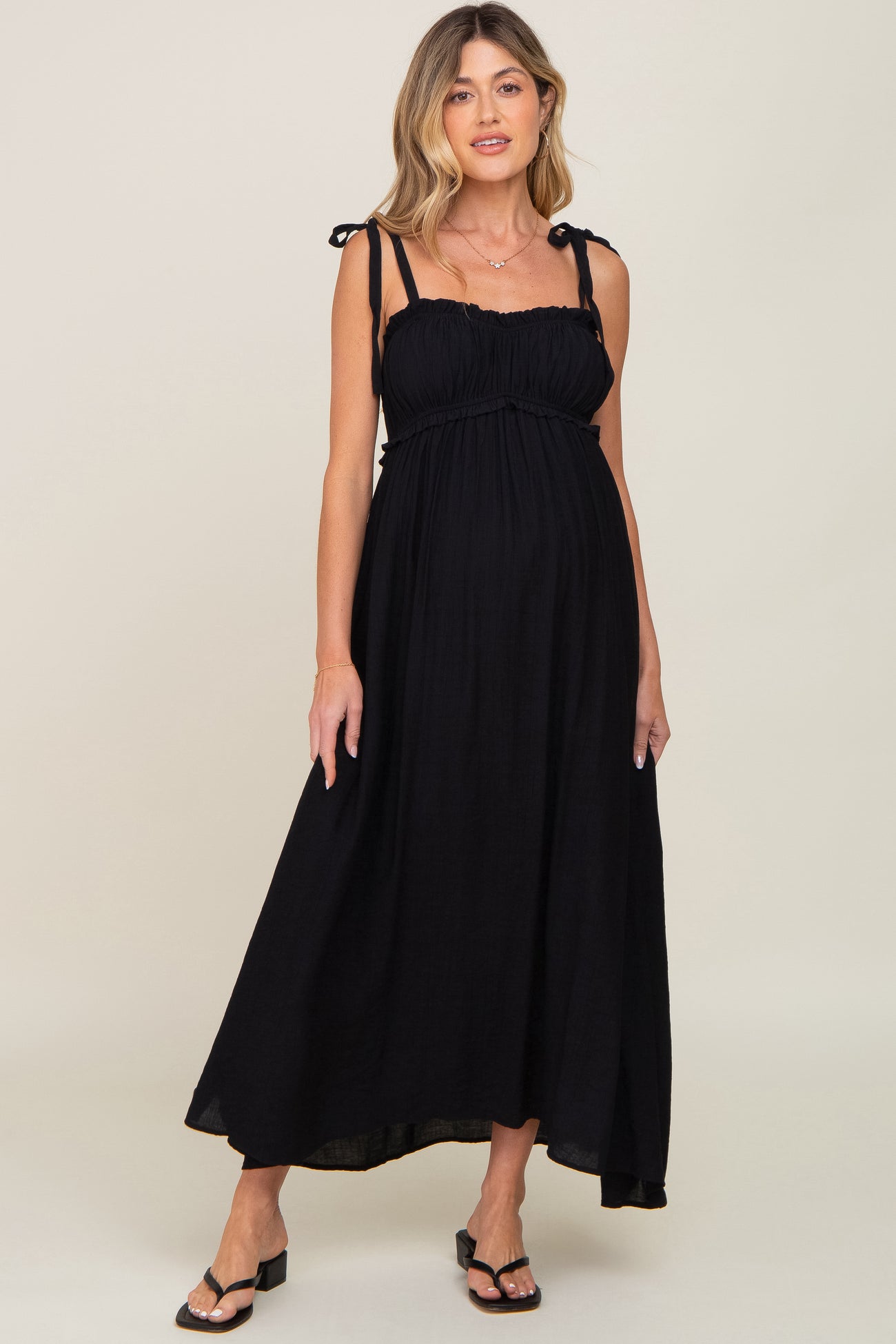 woman wearing a black maternity maxi dress with adjustable tie straps and a flowing silhouette, showing her baby bump