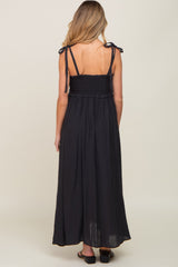 woman wearing a black maternity maxi dress with adjustable straps and a smocked bodice, showing her baby bump from the back