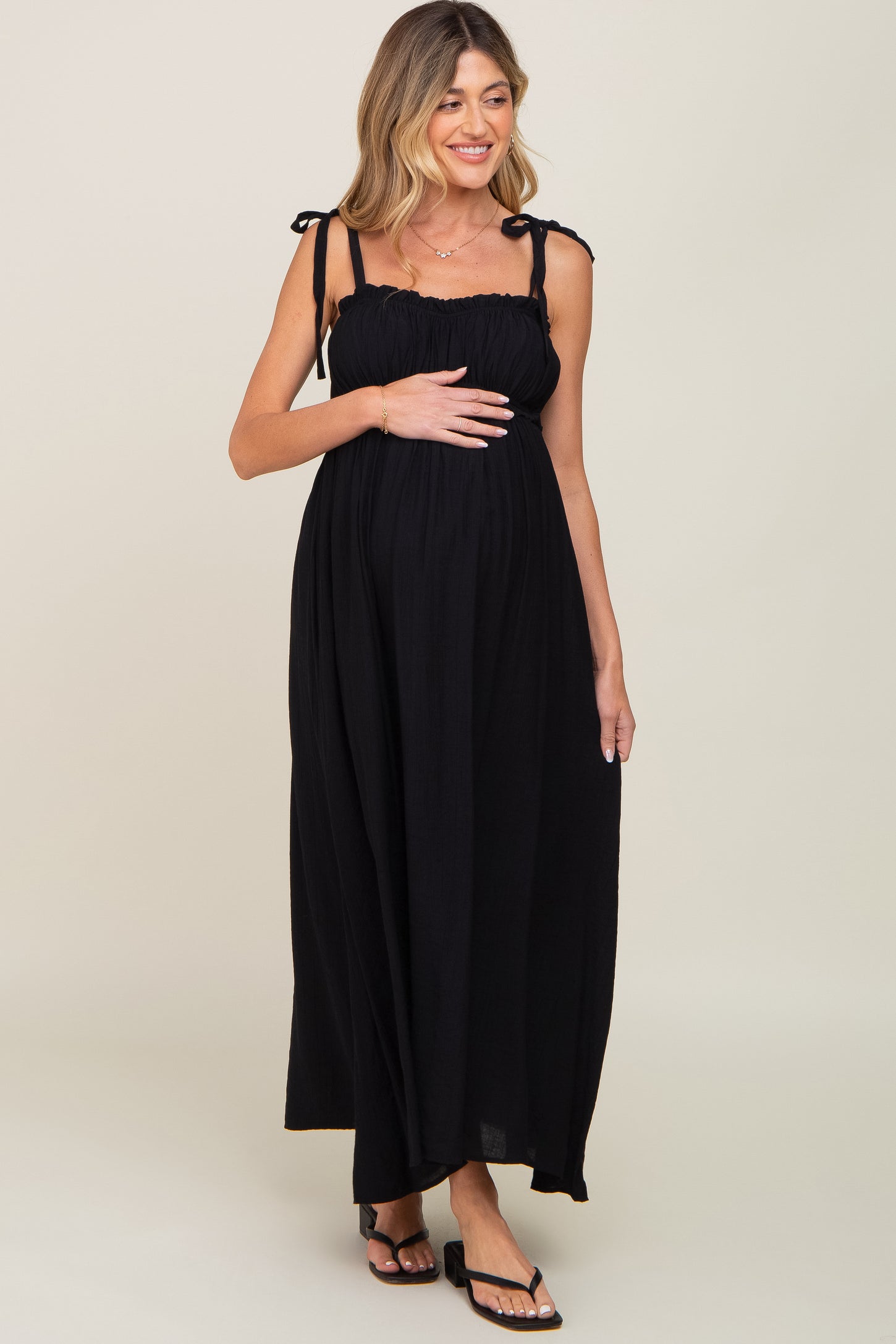 woman wearing a black maternity maxi dress with tie straps and holding her baby bump