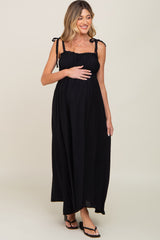 woman wearing a black maternity maxi dress with tie straps and holding her baby bump