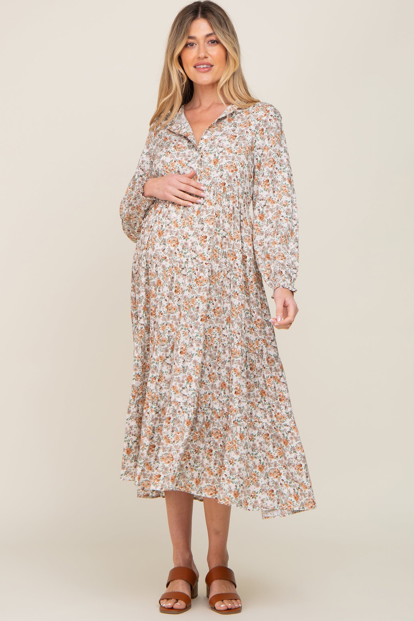 woman wearing a floral midi maternity dress with long sleeves and a collared neckline, holding her baby bump