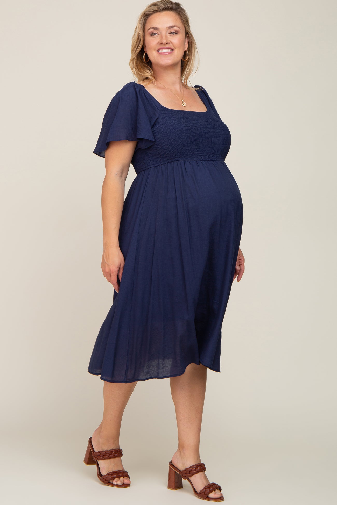 pregnant woman wearing a navy blue smocked maternity midi dress with flutter sleeves and brown heels
