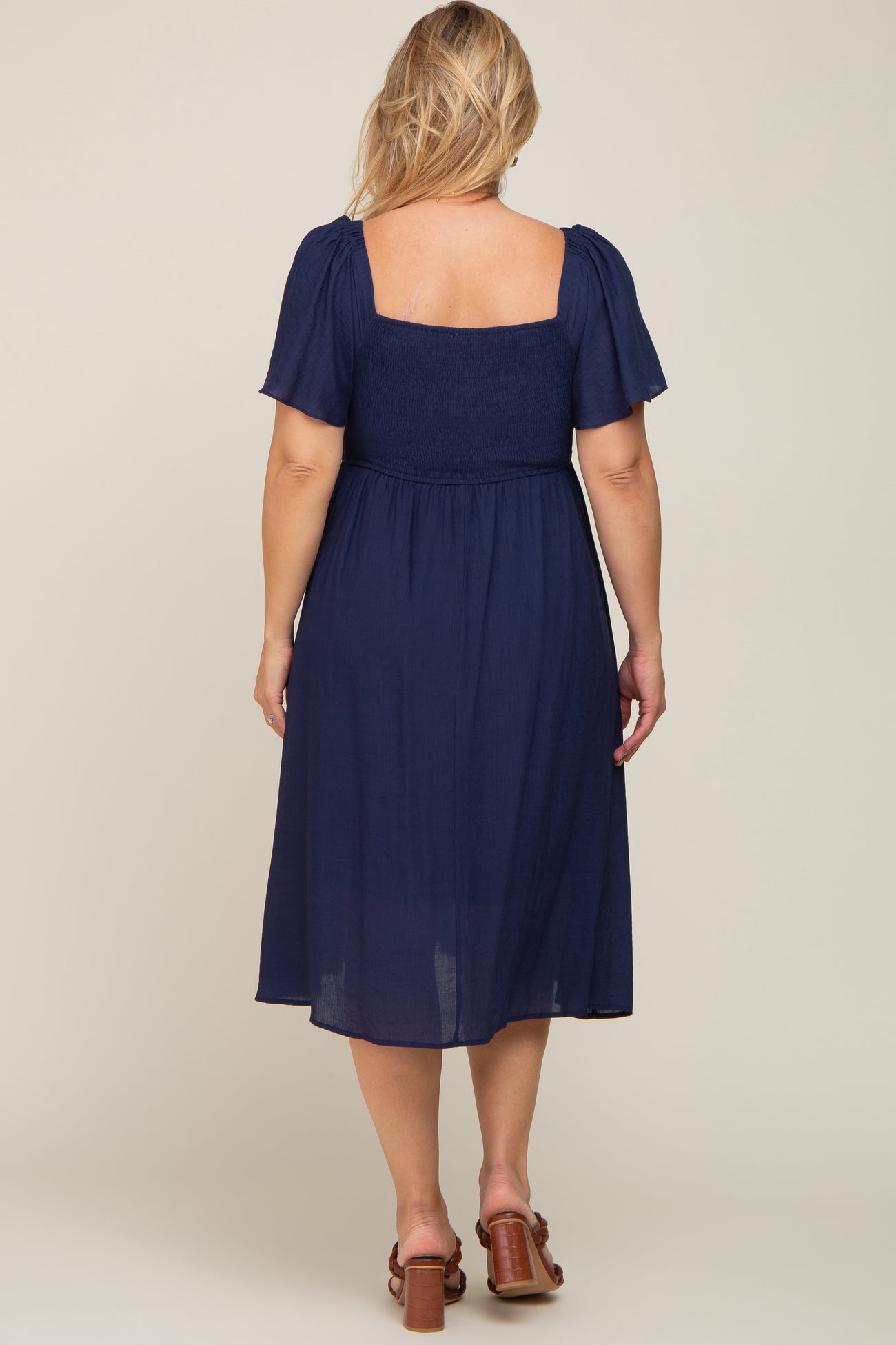 woman wearing a navy blue maternity plus dress with short puff sleeves and a smocked bodice, viewed from the back