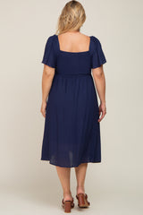 woman wearing a navy blue maternity plus dress with short puff sleeves and a smocked bodice, viewed from the back