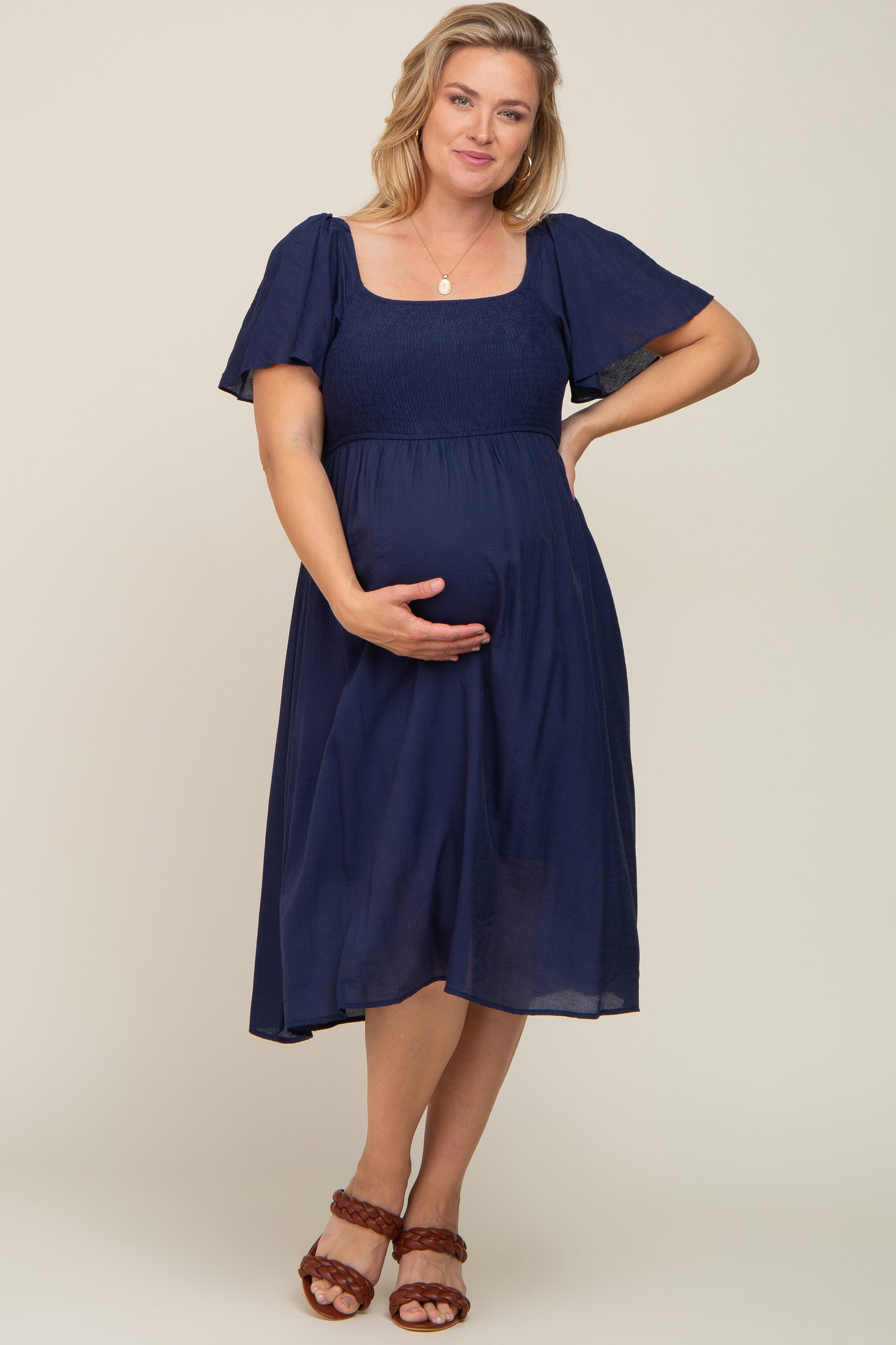 woman wearing a dark navy maternity plus dress with short flutter sleeves and holding her baby bump