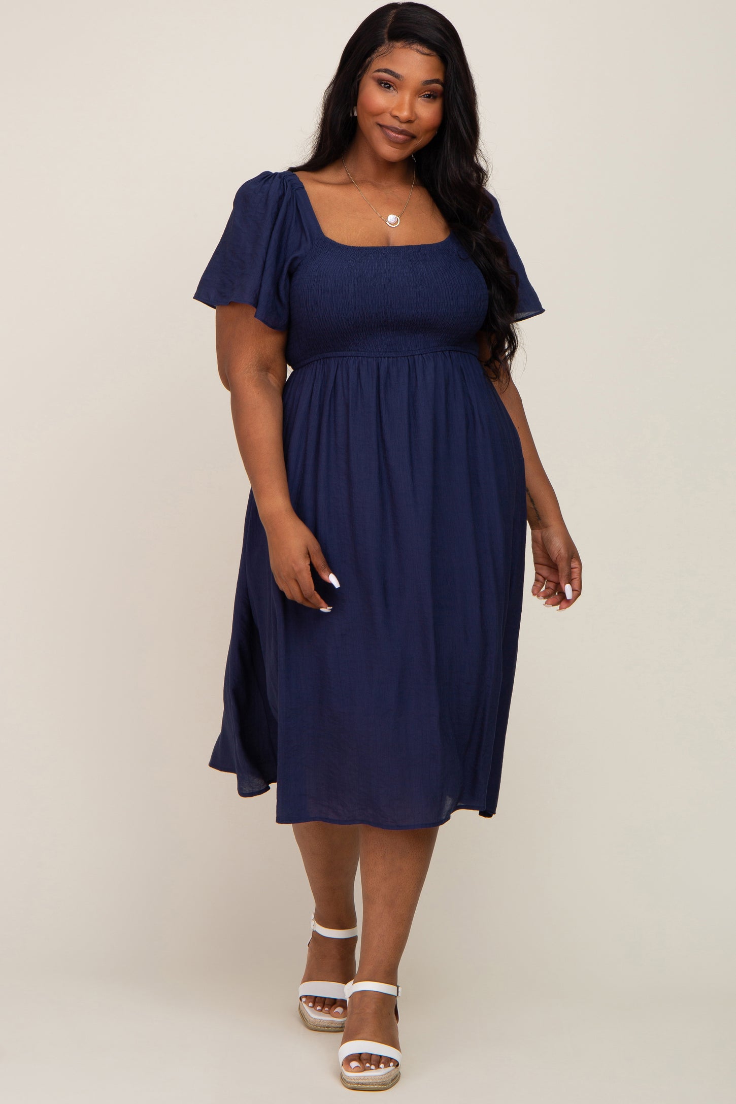 plus size woman wearing a navy blue smocked midi dress with flutter sleeves and white sandals