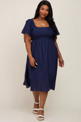 plus size woman wearing a navy blue smocked midi dress with flutter sleeves and white sandals