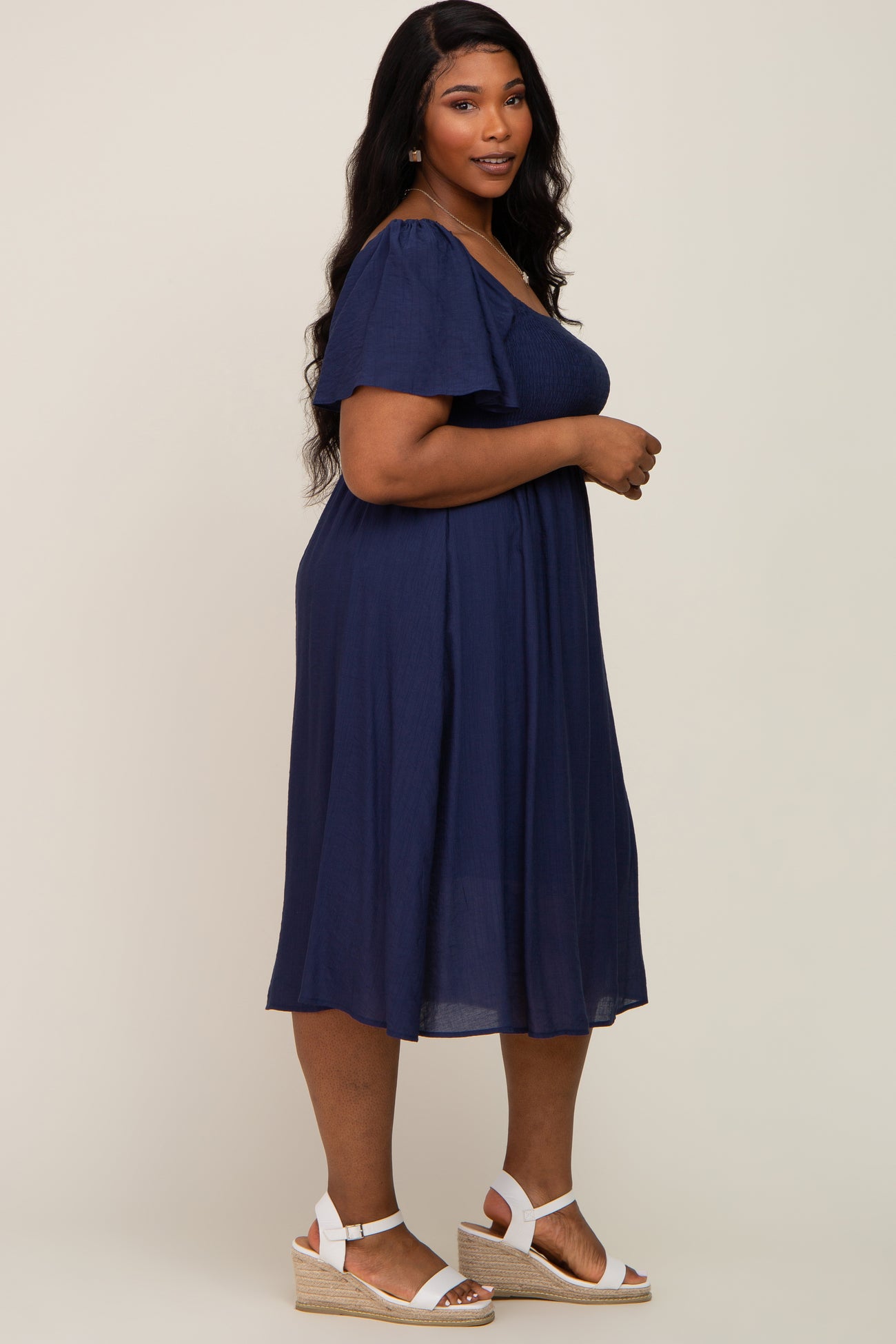 woman wearing a navy blue plus size dress with short flutter sleeves and wedge sandals