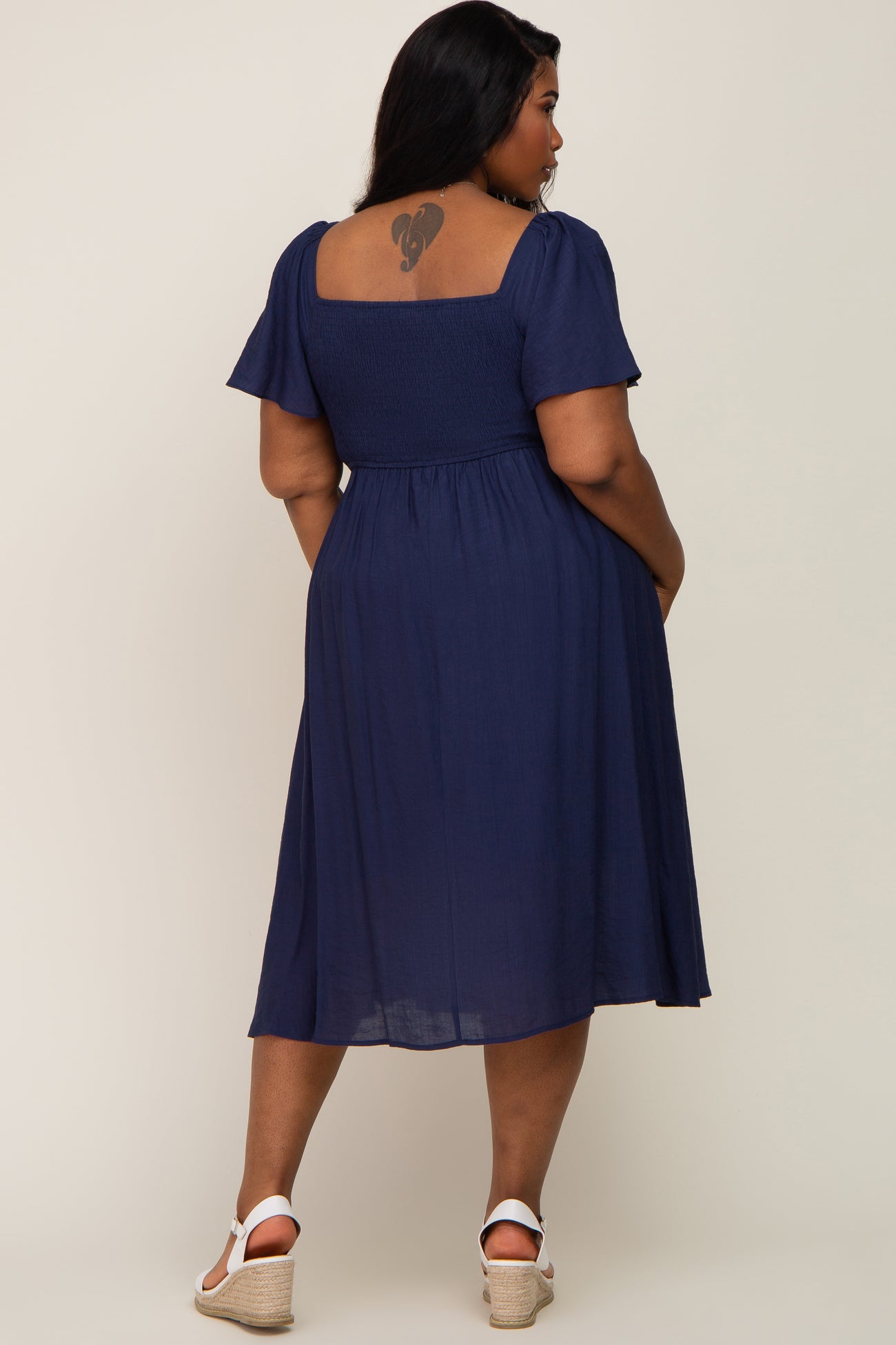 woman wearing a navy blue plus-size midi dress with short sleeves and a smocked bodice, showing a back view