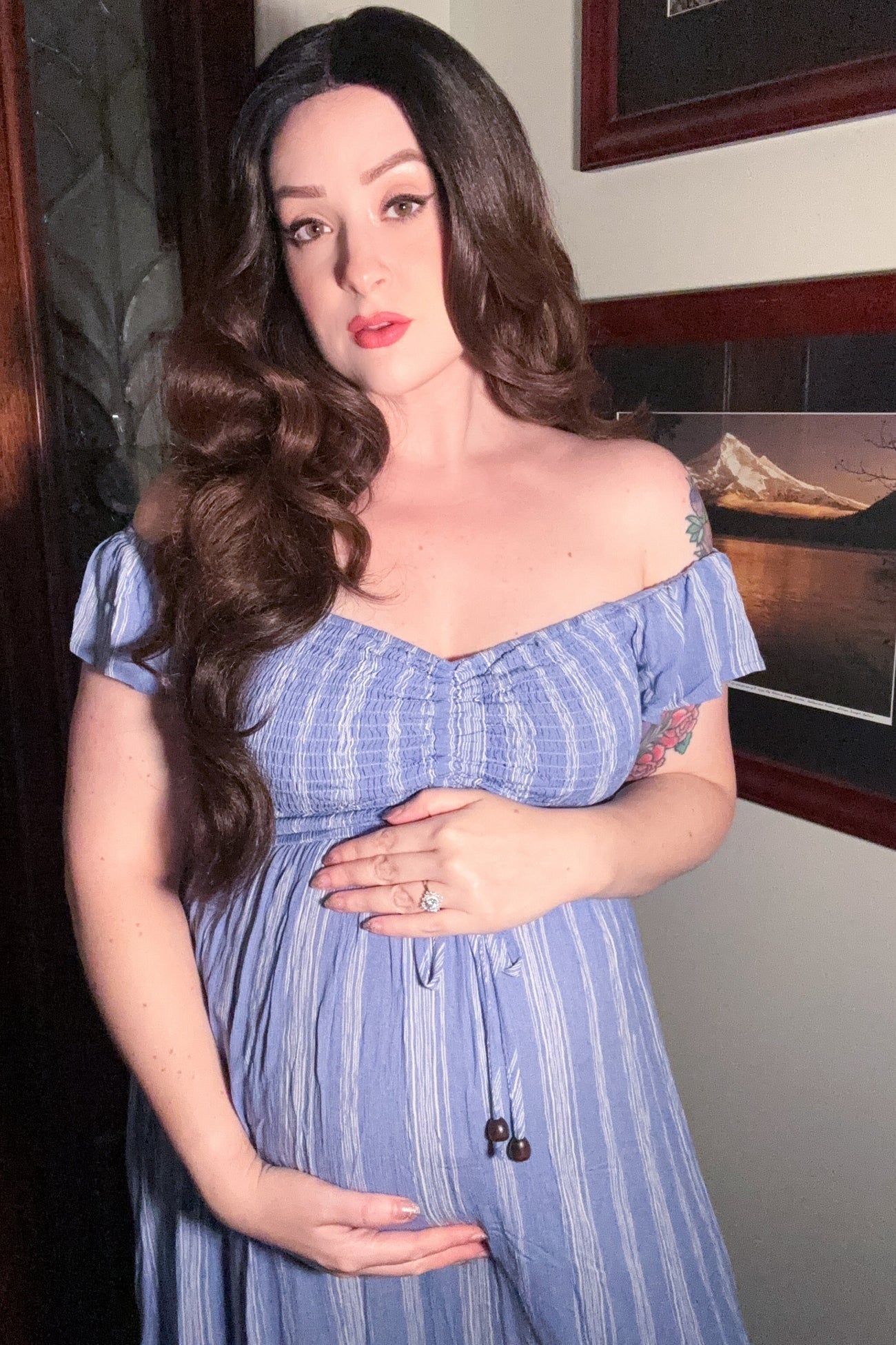 woman wearing a blue striped off-the-shoulder maternity dress and holding her baby bump