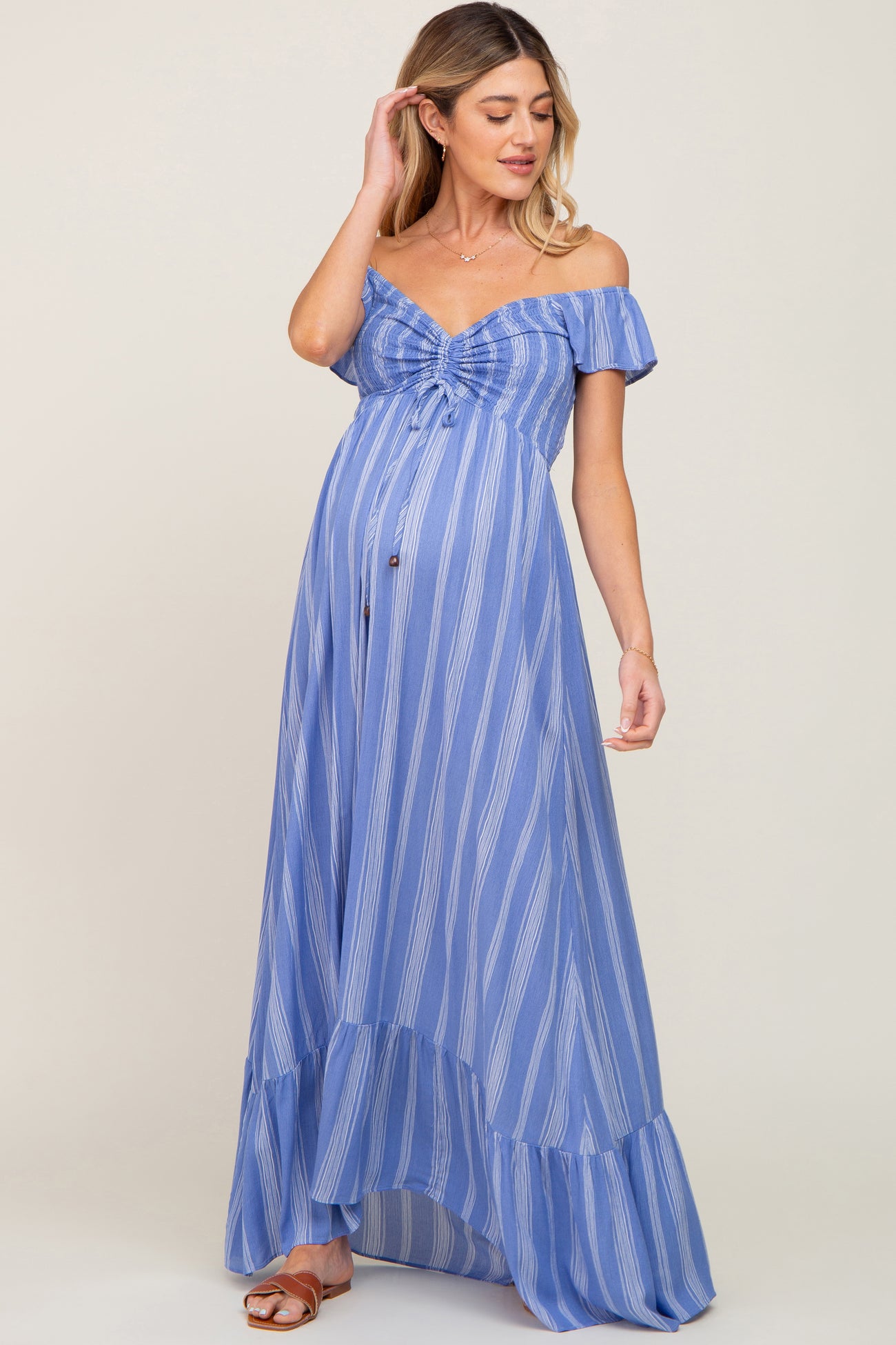 woman wearing a blue striped off-the-shoulder maternity dress with a flowing hem and visible baby bump