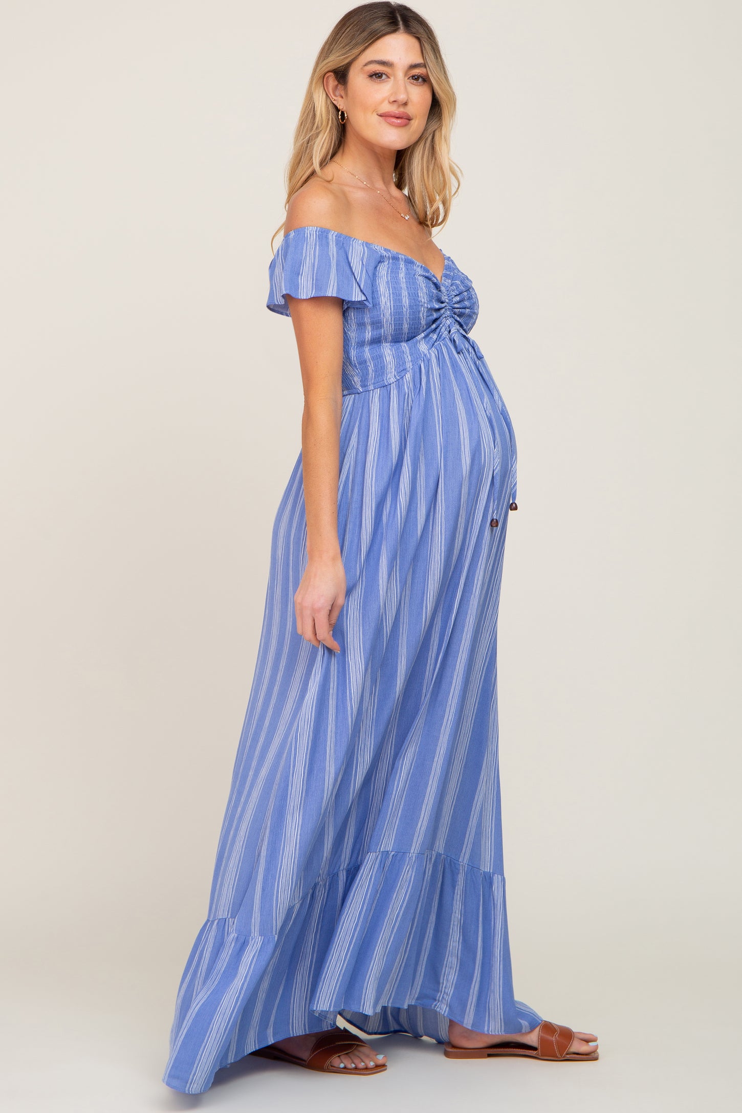 woman wearing a blue and white striped off-the-shoulder maternity maxi dress with a visible baby bump