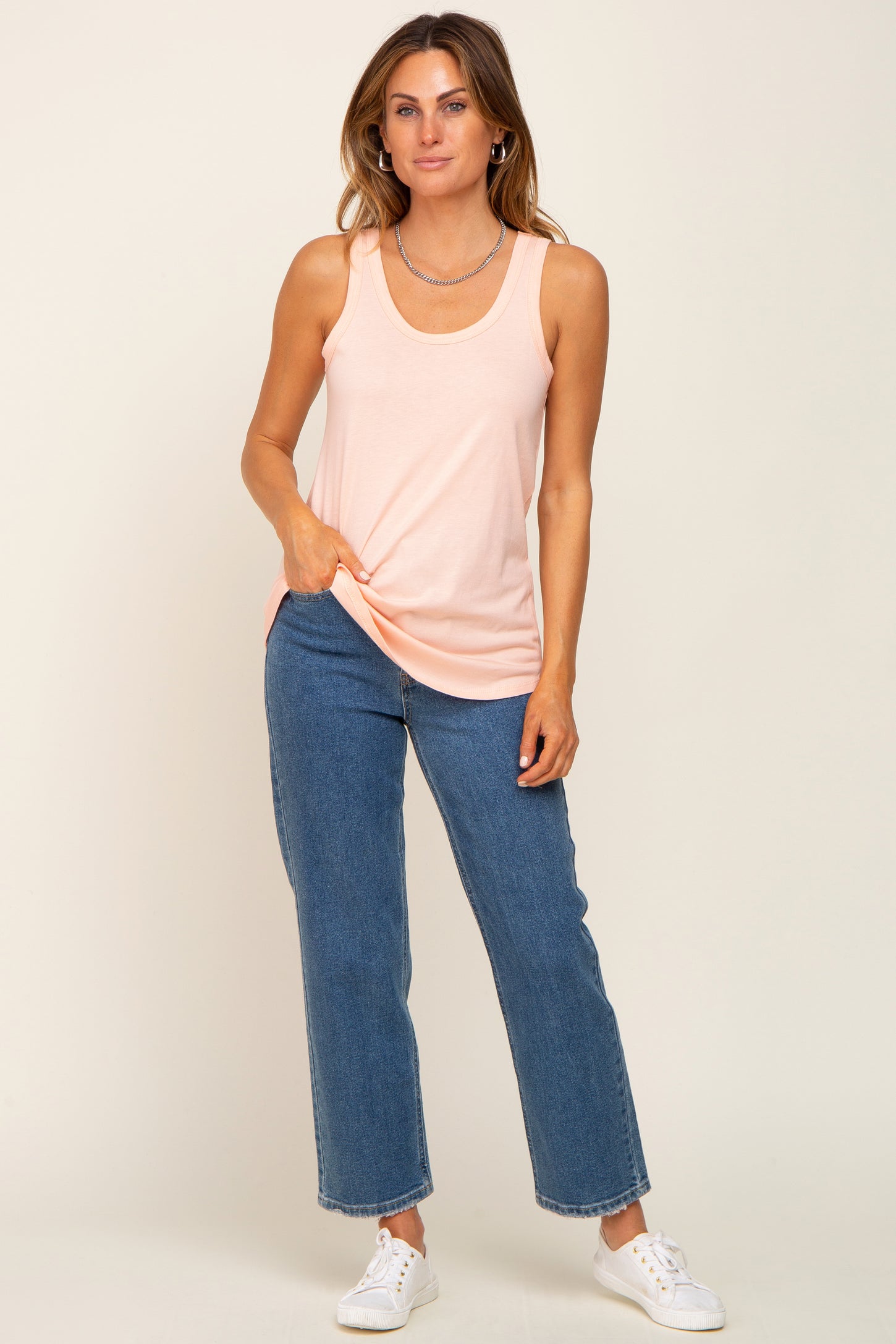 woman wearing a light peach sleeveless tank top and blue wide-leg jeans with white sneakers