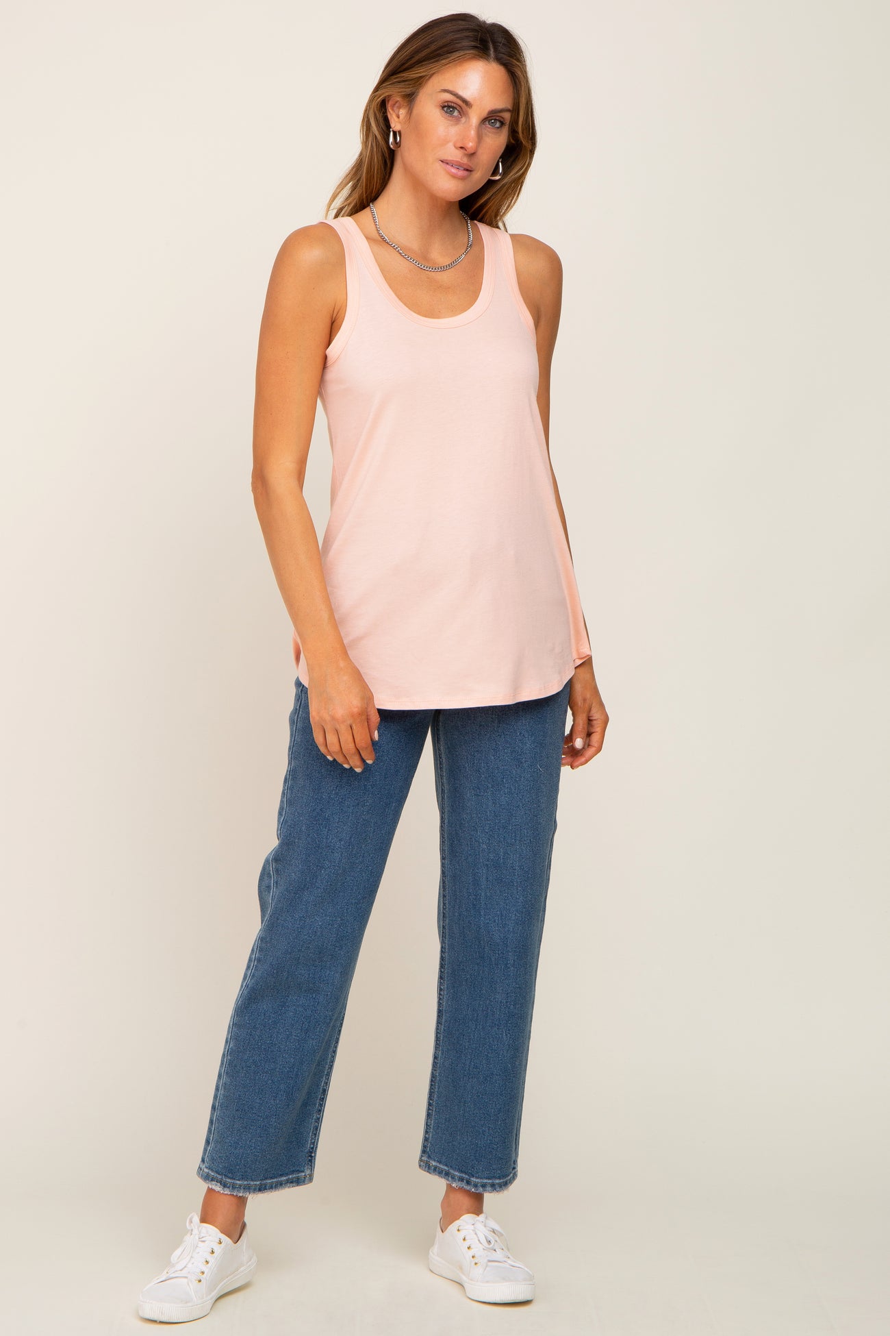 woman wearing a light pink sleeveless top paired with high-waisted wide-leg jeans and white sneakers